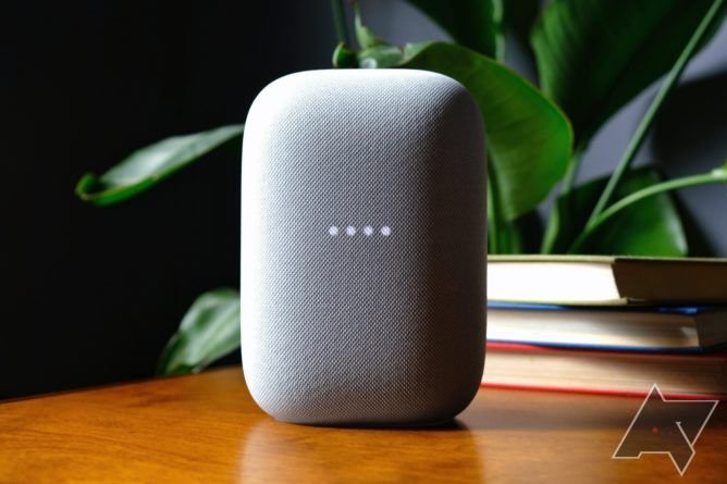 A Google Nest Audio Speaker on a table with books and a plant in the background